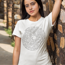 Load image into Gallery viewer, Woman wearing a white t-shirt with text leaning against a stone wall.