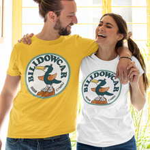Load image into Gallery viewer, A man and a woman standing arm-in-arm in front of a yellow window, wearing matching Bilidowcar t-shirts. The man wears a bright yellow t-shirt with a circular blue and orange bird graphic, and the woman wears a white t-shirt with the same graphic.